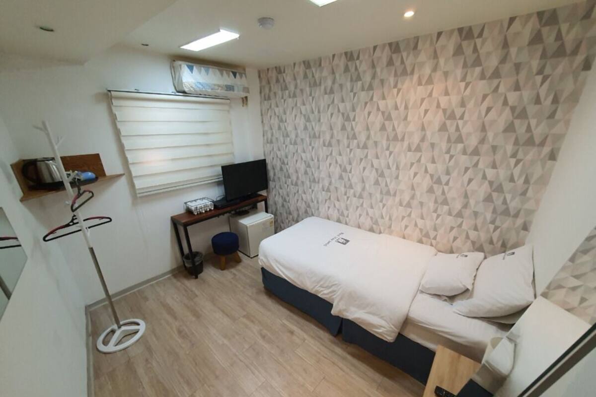 A compact bedroom with a bed, a desk with a computer, a television, and a wall-mounted air conditioner.