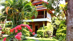 A traditional multi-story building with a balcony, surrounded by lush greenery and a stone pathway leading to the entrance. - Puri Cendana Resort Bali (Seminyak)