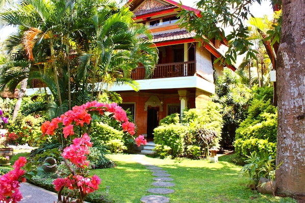 A traditional multi-story building with a balcony, surrounded by lush greenery and a stone pathway leading to the entrance. - Puri Cendana Resort Bali (Seminyak)