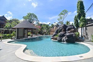 A swimming pool with a waterfall feature, surrounded by lounge chairs and a gazebo. - Puri Cendana Resort Bali (Seminyak)