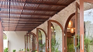 A covered outdoor seating area with wooden tables and chairs, stone walls, and potted plants. - Puri Cendana Resort Bali (Seminyak)