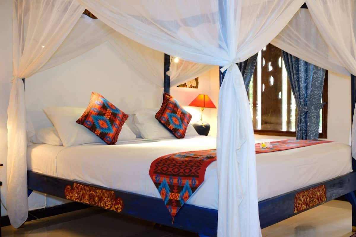 A bed with a canopy, pillows, a lamp, and a window with curtains.