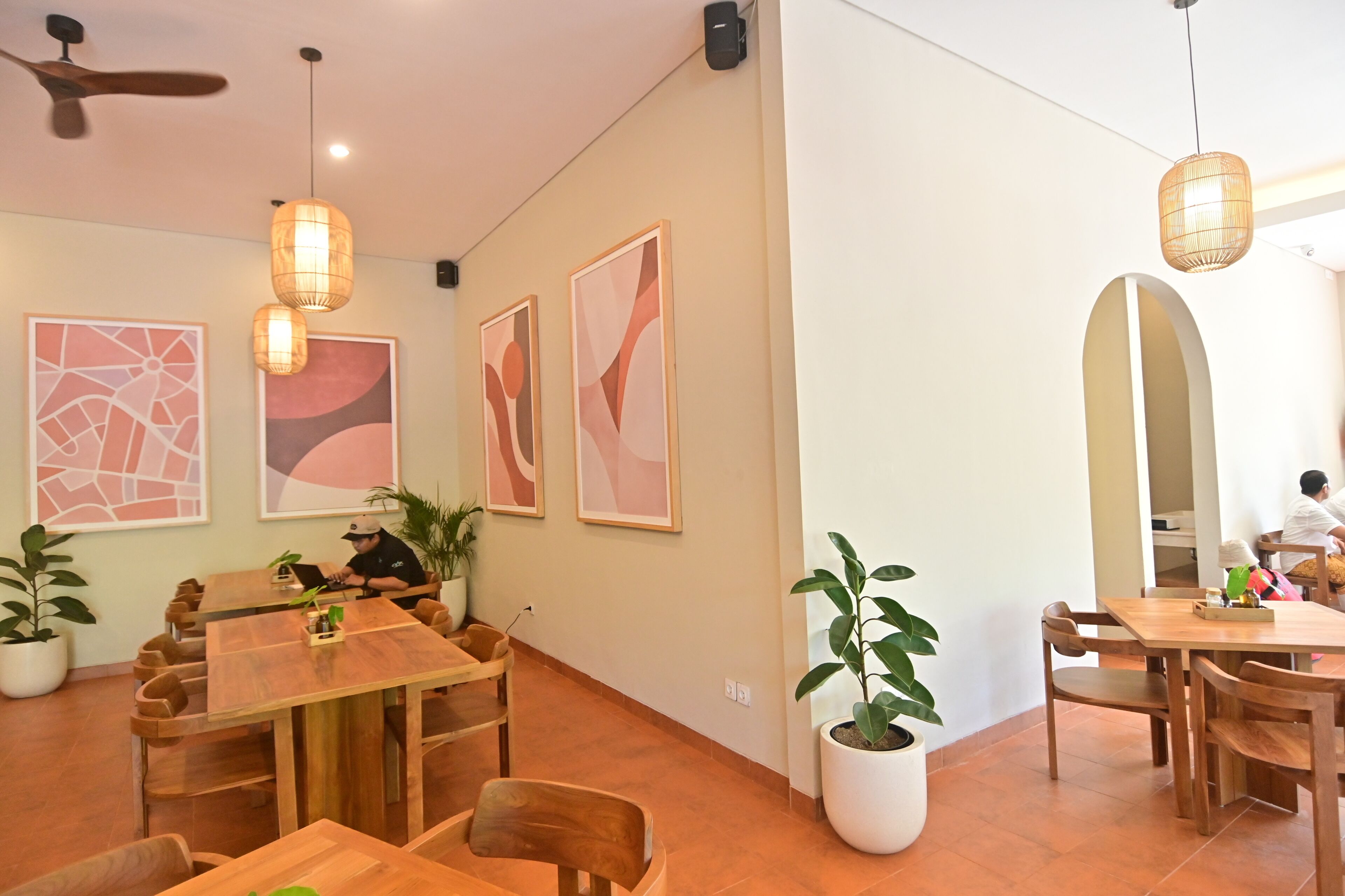 A modern dining area with wooden tables and chairs, potted plants, and abstract wall art.