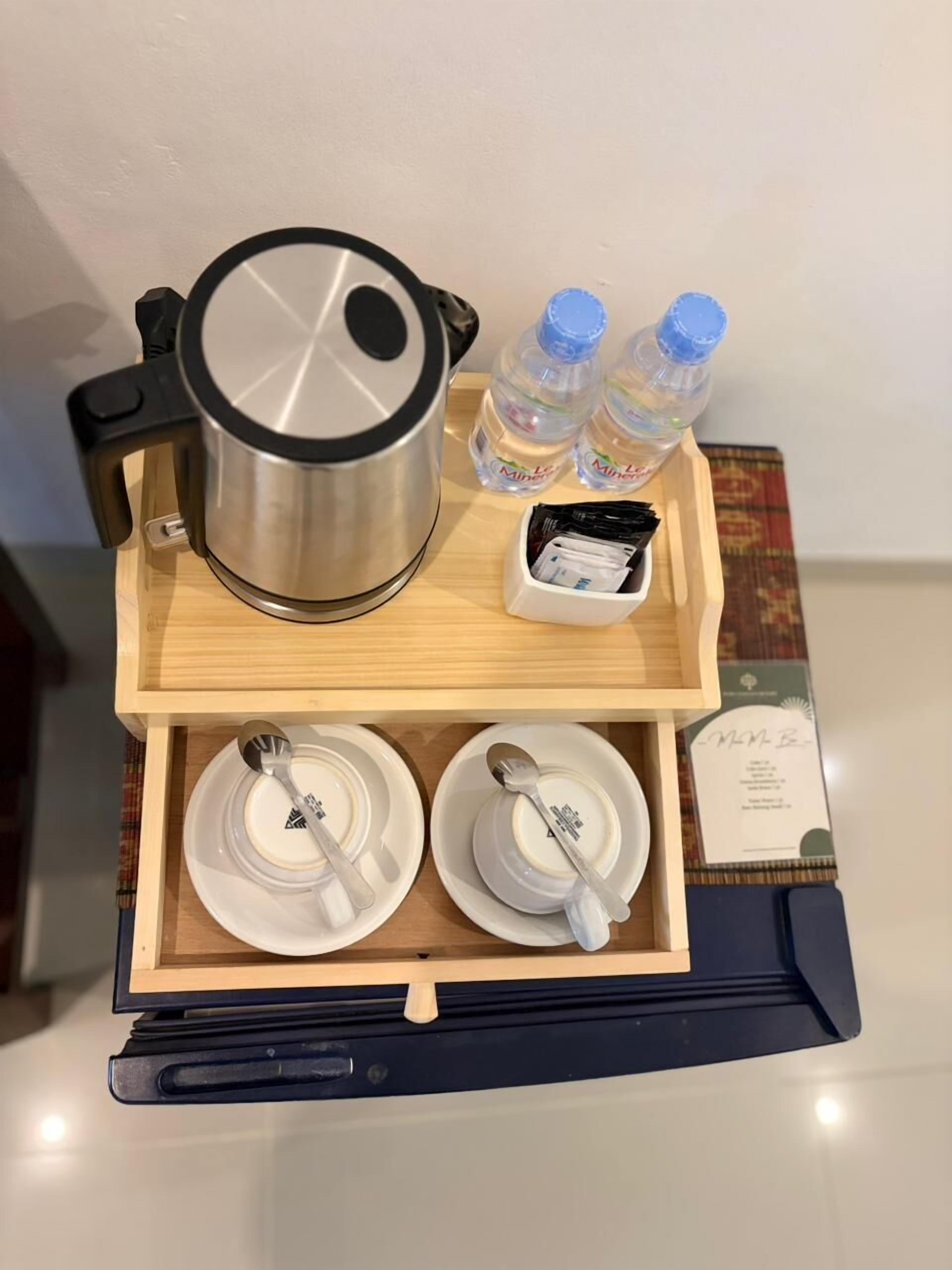 A tray with a stainless steel pot, two water bottles, a white cup, and a small white box containing items.