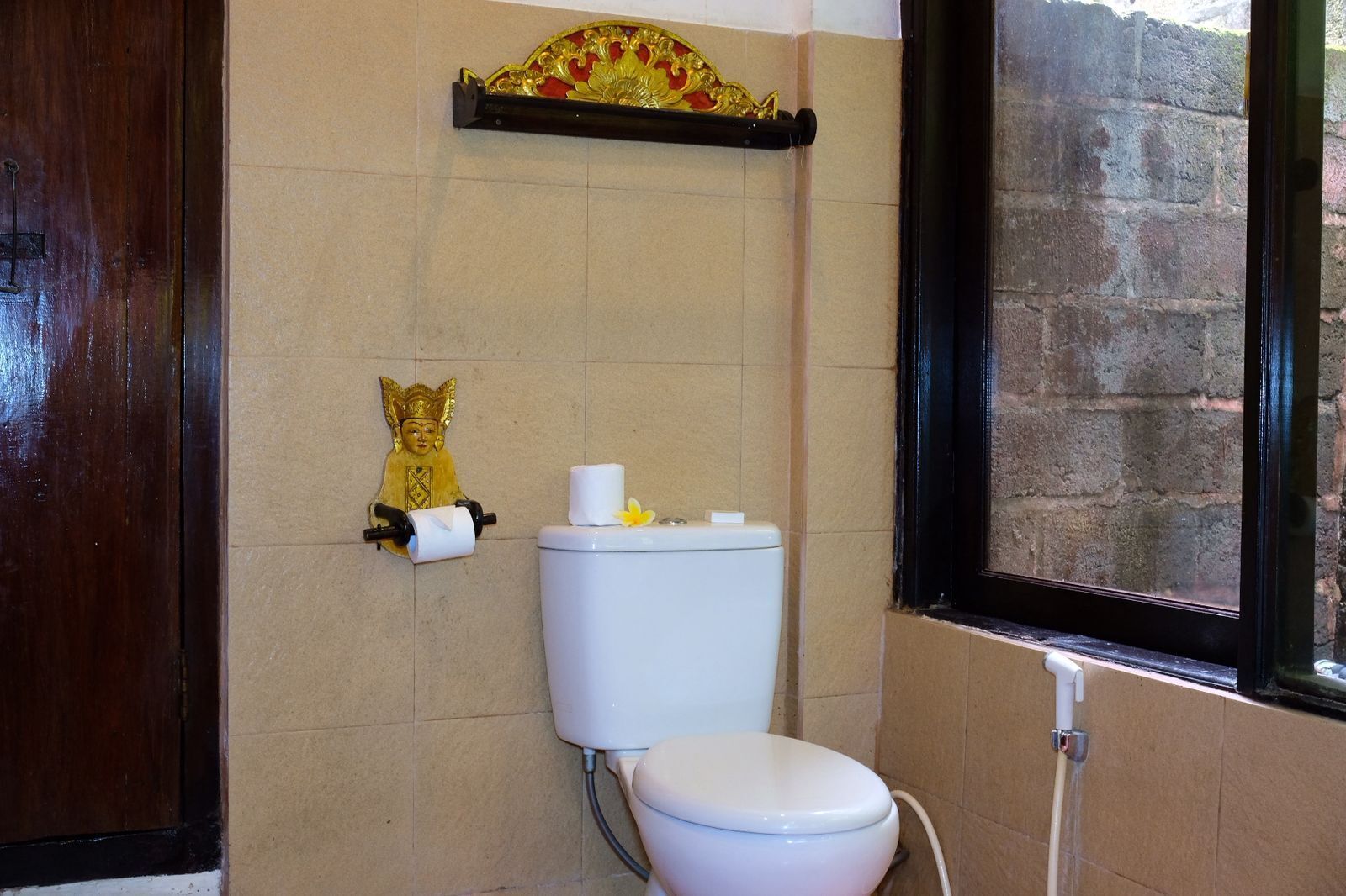A bathroom with a toilet, a toilet paper holder, and a decorative golden figure on the wall.