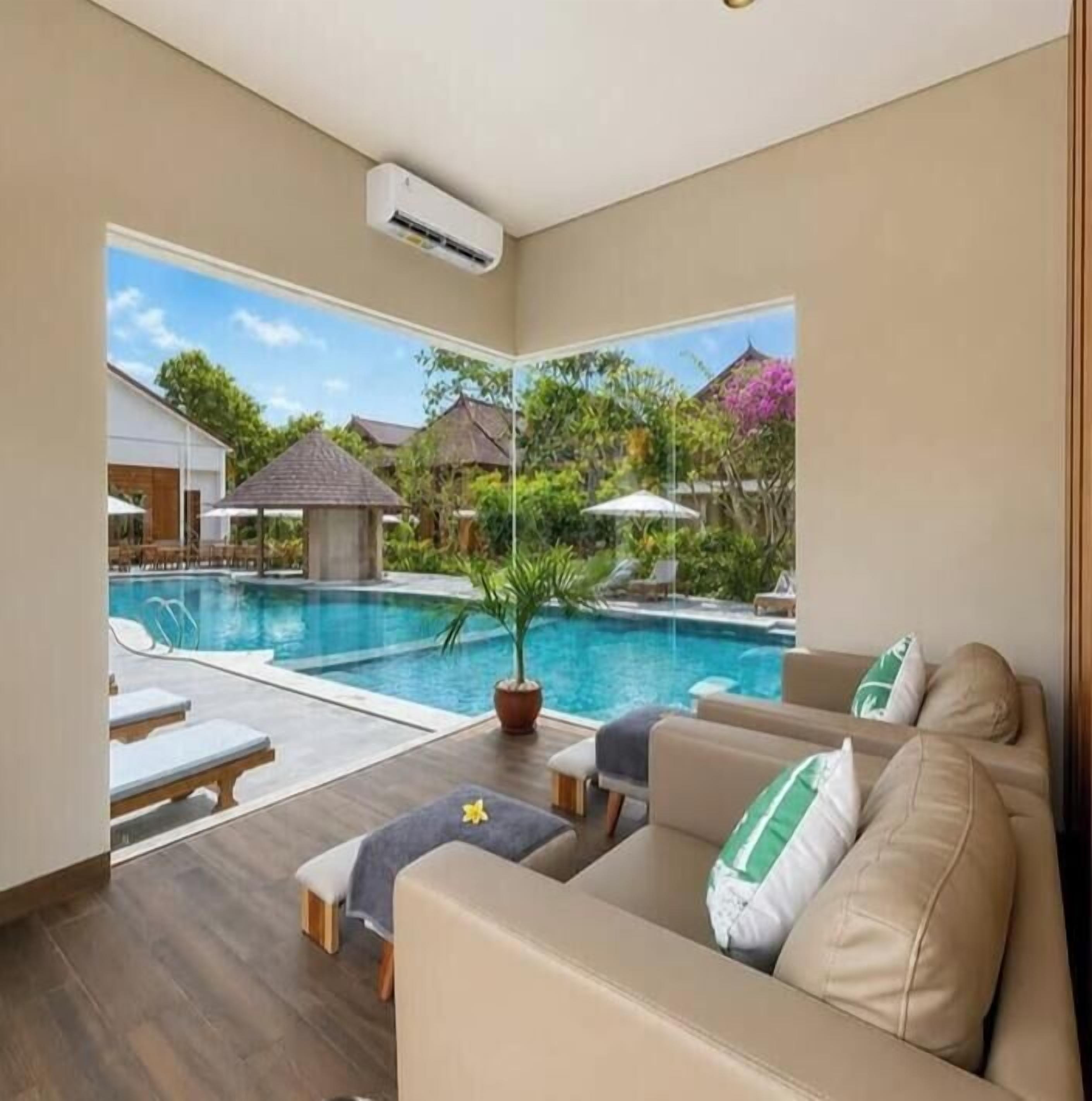 A room with a view of a swimming pool, a sofa, and a potted plant.