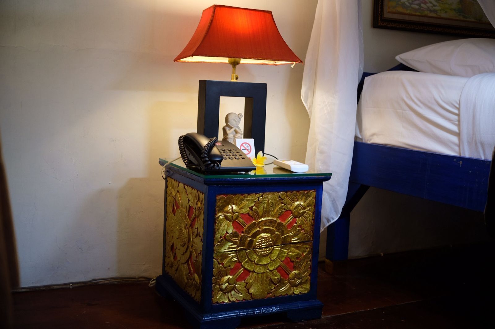 Une table de chevet avec une lampe, un téléphone et un petit objet décoratif.