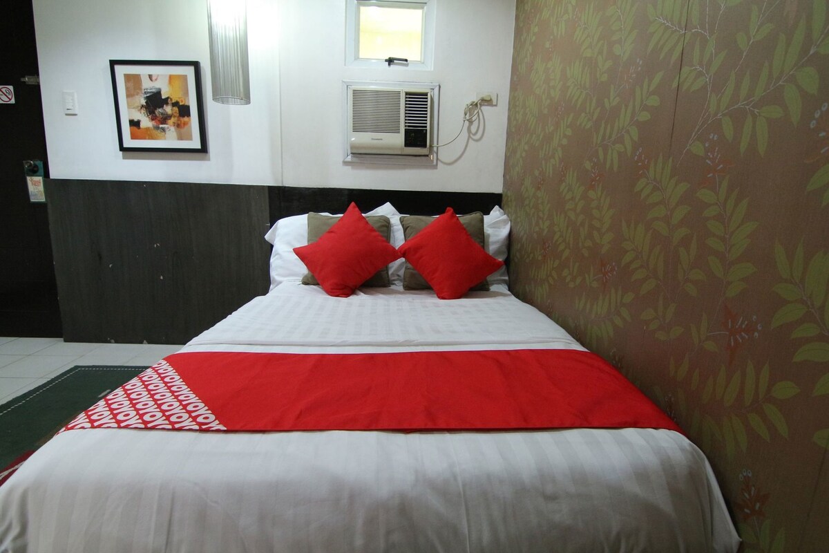 A hotel room with a bed, a wall-mounted air conditioner, a framed picture, and a patterned wall.
