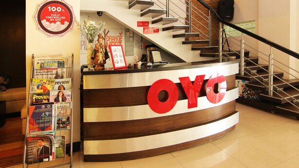 Bancada de recepção com um grande logotipo 'OYG', uma escadaria e um suporte de revistas com diversas publicações.