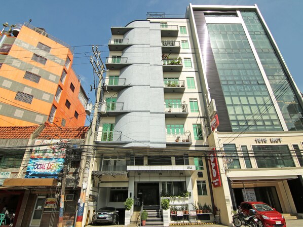A multi-story building with balconies, a car parked in front, and a sign indicating '1818 LMT'.