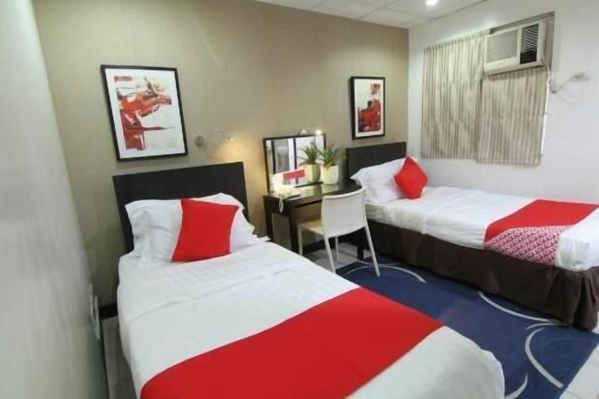 Una habitació d'hotel amb dos llits, cadascun amb llençol vermell i blanc, una taula de treball amb una cadira, i dos quadres a la paret.