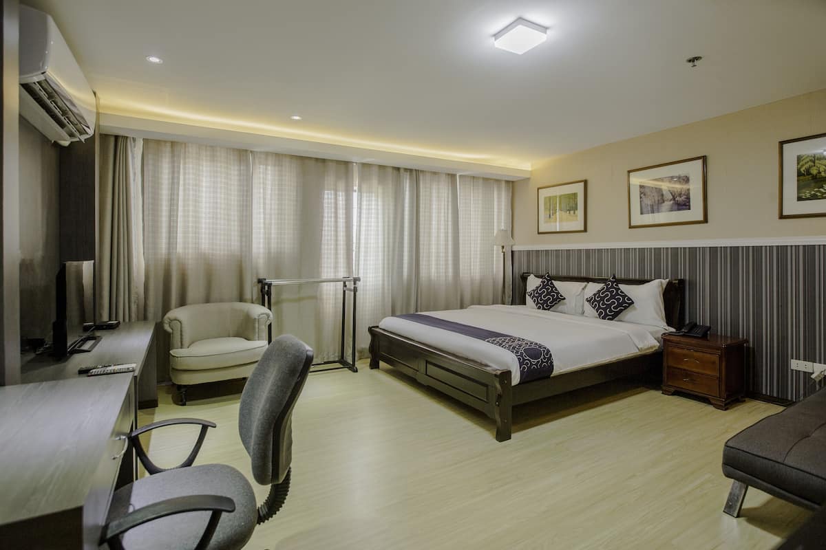 A hotel room with a bed, a desk, a chair, a bedside table, and a TV.