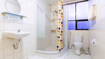A bathroom with a shower, toilet, sink, and a window with a towel hanging on the wall.