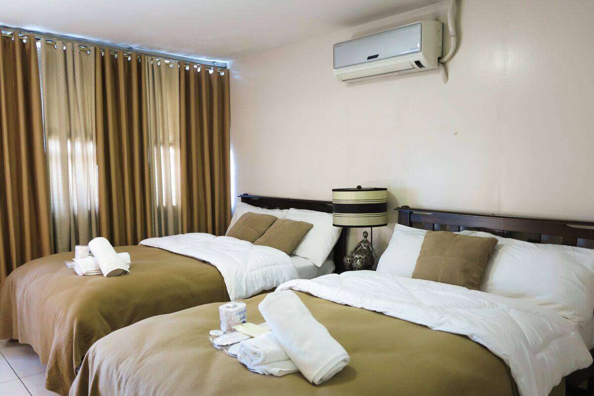 A hotel room with two beds, beige bedding, a bedside lamp, and a window with curtains.