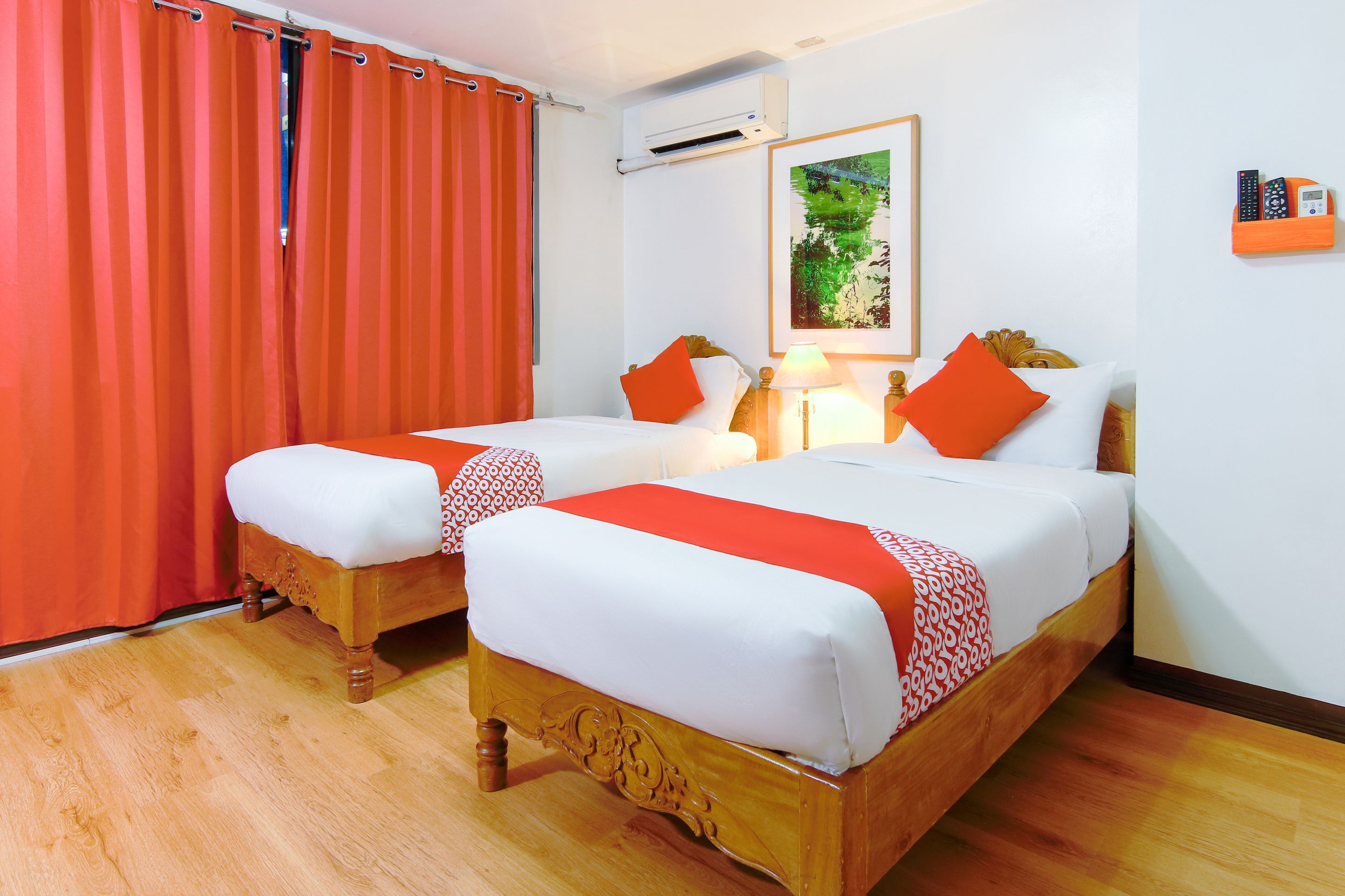 Habitación de hotel con dos camas de madera, cortinas rojas, un cuadro en la pared y un equipo de aire acondicionado.
