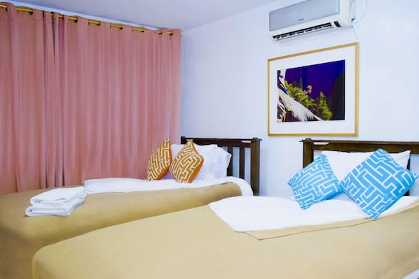 A hotel room with two beds, a framed picture on the wall, and an air conditioning unit.