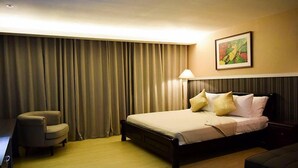 A hotel room with a bed, a chair, a desk, a lamp, and a painting on the wall. - Newgrange Condotel (Quezon City)