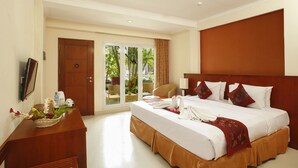 Habitación de hotel con una cama grande, un escritorio de madera, un televisor y un balcón con vistas a zonas verdes.