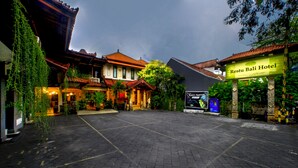 Un patio con arquitectura tradicional, un letrero del Hotel Resto Bali y un cartel publicitario de una película.
