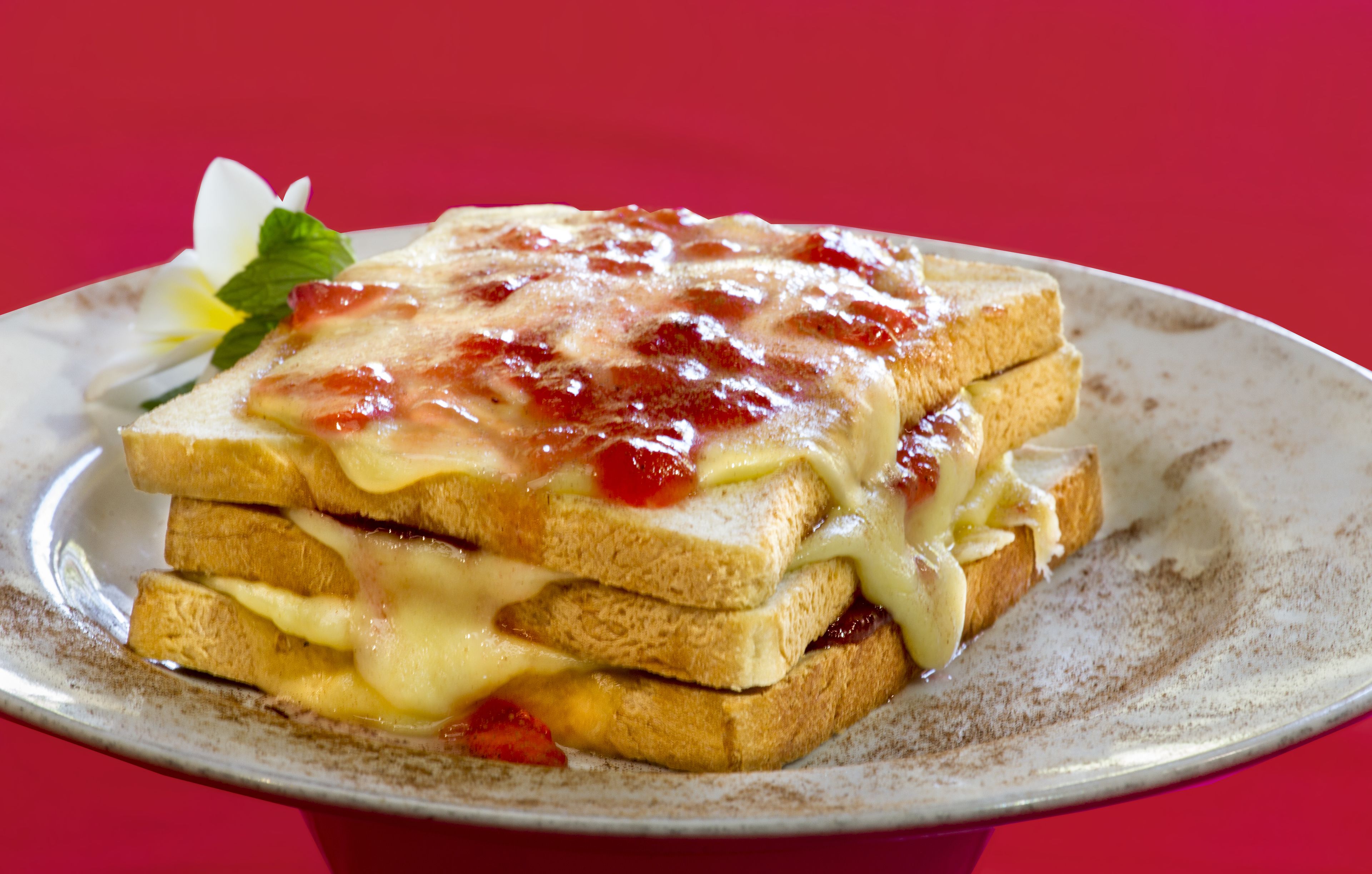A plate with a stack of toast sandwiches topped with melted cheese and jam.