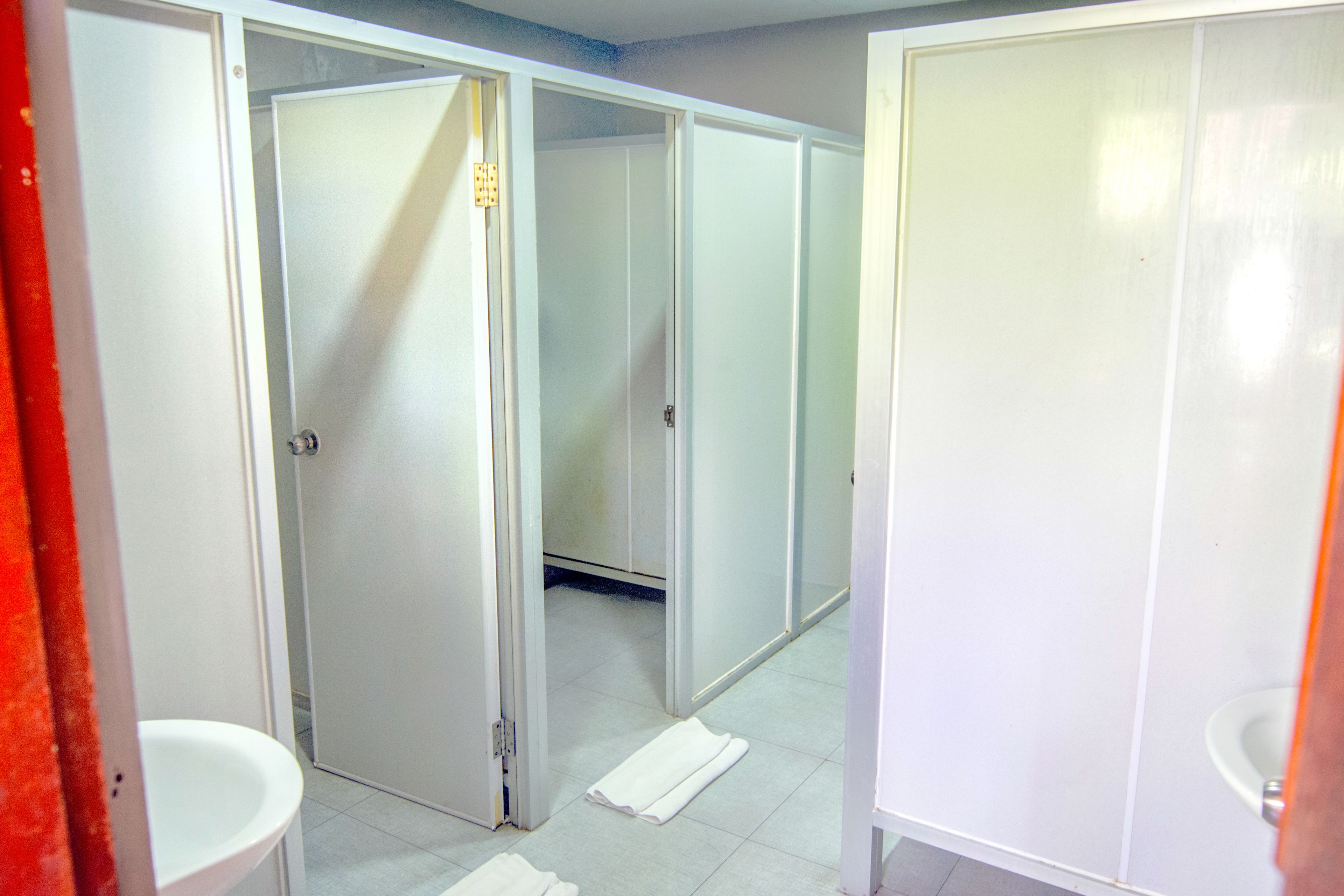 A hotel bathroom with multiple stalls, a sink, and a mirror.