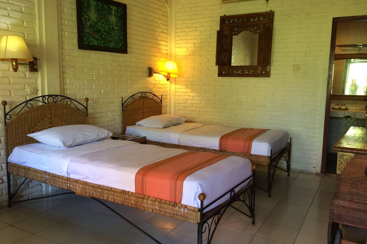 A room with two beds, a wooden headboard, a mirror, and a wall-mounted lamp.