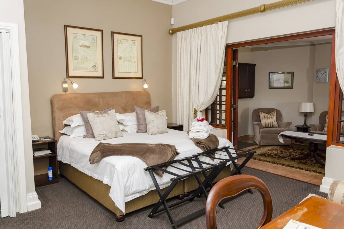 Habitación de hotel con cama, escritorio, silla y vista al área de estar a través de una puerta abierta.