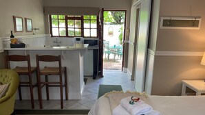 A hotel room with a bed, a small desk, two chairs, a kitchenette, and a view of the outdoor area. - Brighton Lodge (Gqeberha (Port Elizabeth))