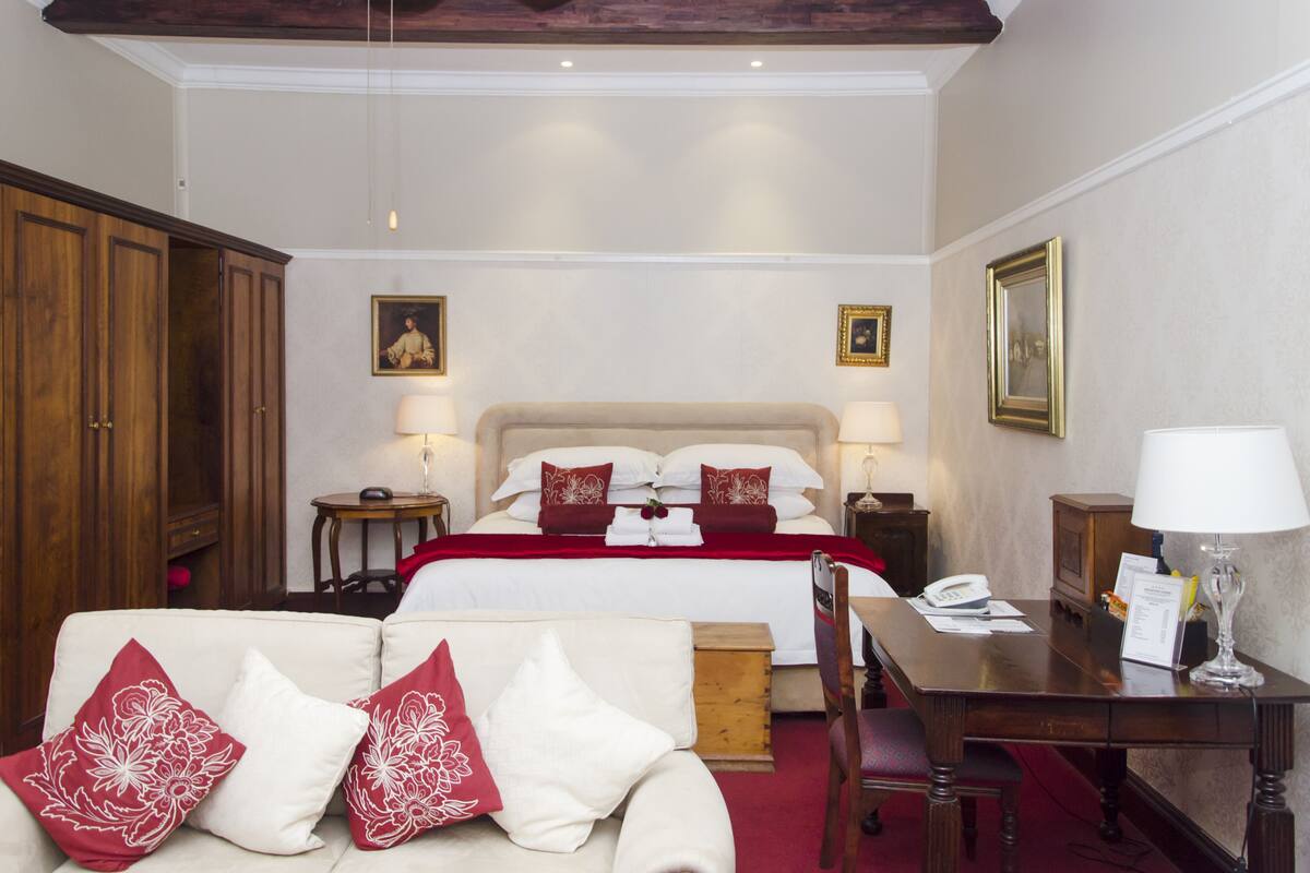 Habitación de hotel con cama, mesitas de noche, escritorio, silla, sofá y armario.