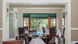 A dining area with tables set for four, surrounded by chairs, with a view of a pool and greenery outside. - Brighton Lodge (Gqeberha (Port Elizabeth))