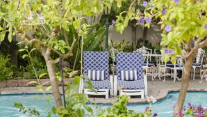 A poolside area with lounge chairs and a table, surrounded by greenery and a white fence. - Brighton Lodge (Gqeberha (Port Elizabeth))