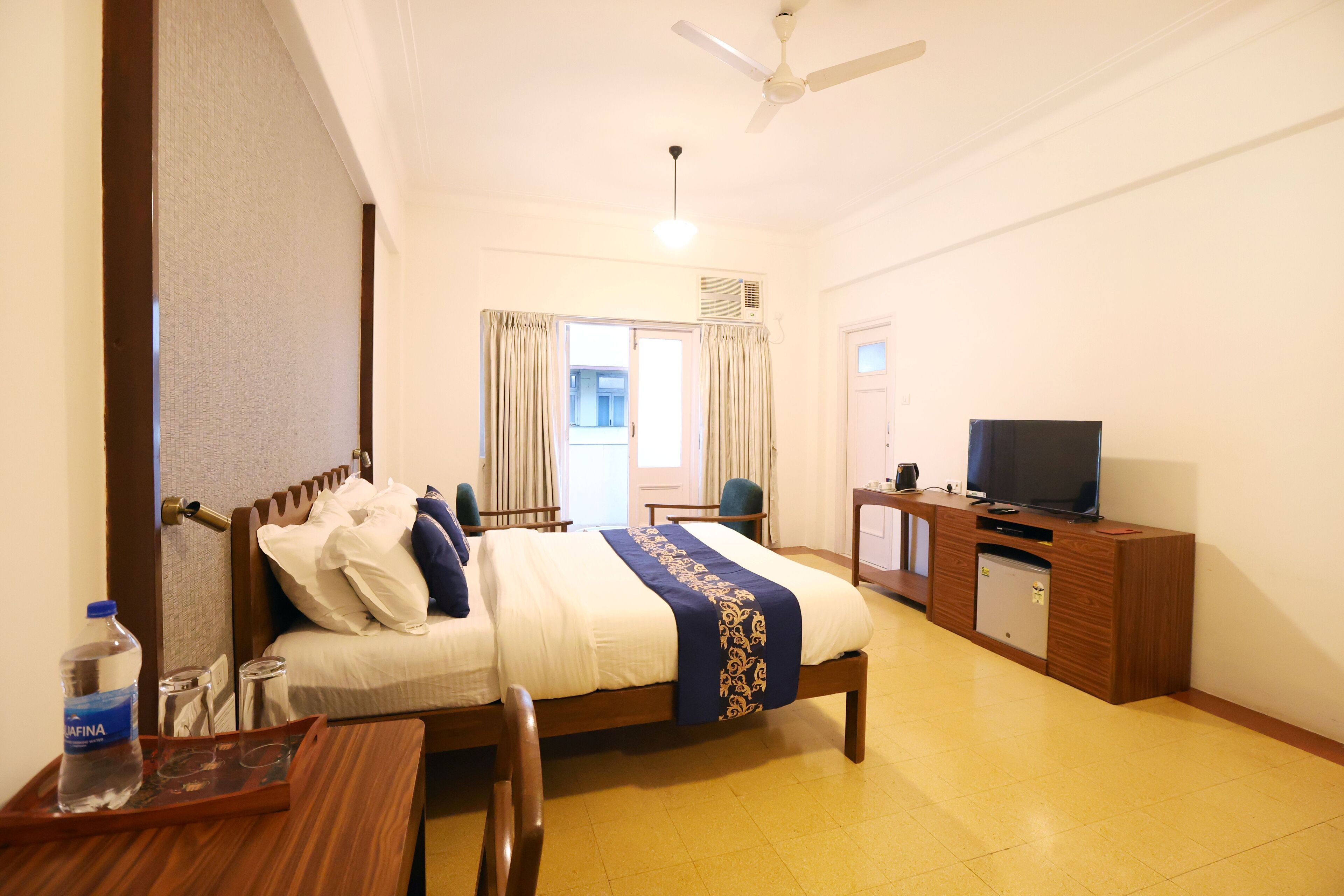 A hotel room with a bed, a desk with a chair, a television, and a ceiling fan.