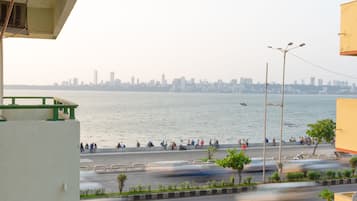 A waterfront view with a city skyline in the background, a road with moving vehicles, and a pedestrian walkway with people.