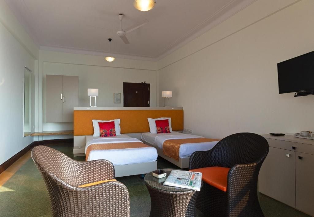 A hotel room with two beds, a television, a desk, and wicker furniture.