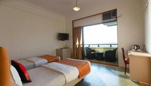 A hotel room with two beds, a TV, a desk with a chair, and a balcony with a view. - Sea Green Hotel (Mumbai)
