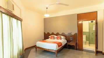 A hotel room with a bed, a ceiling fan, a nightstand, a wooden door, and a shower area.