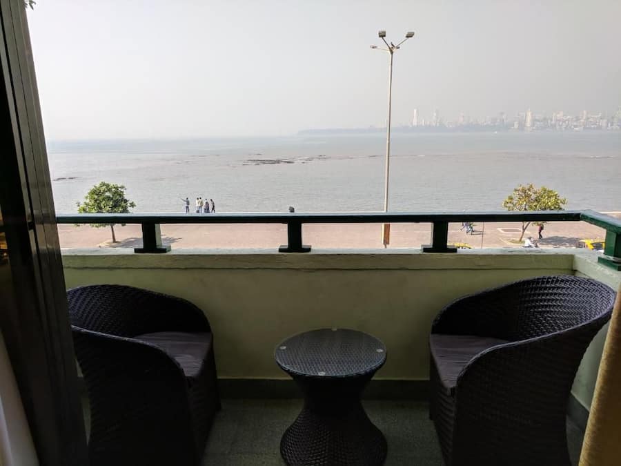 A balcony with wicker furniture and a view of the sea and city skyline.