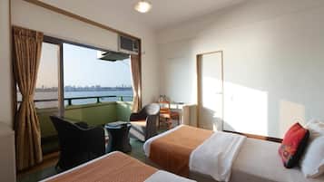 Habitación de hotel con dos camas, un escritorio, una silla y vista a un horizonte urbano a través de amplias ventanas.