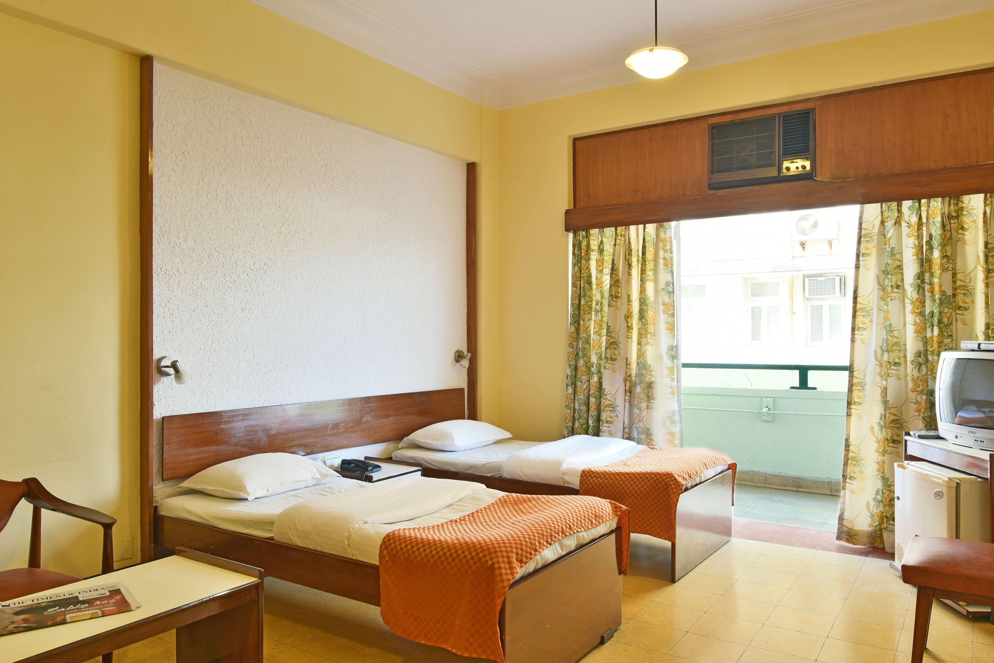Een hotelkamer met twee bedden, een kleine tafel, een stoel, een televisie en een raam met gordijnen.
