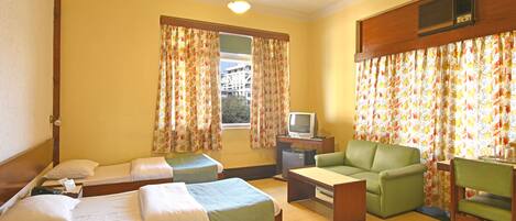Una habitación con dos camas individuales, un sofá verde, una mesita, un televisor y cortinas con estampado floral.