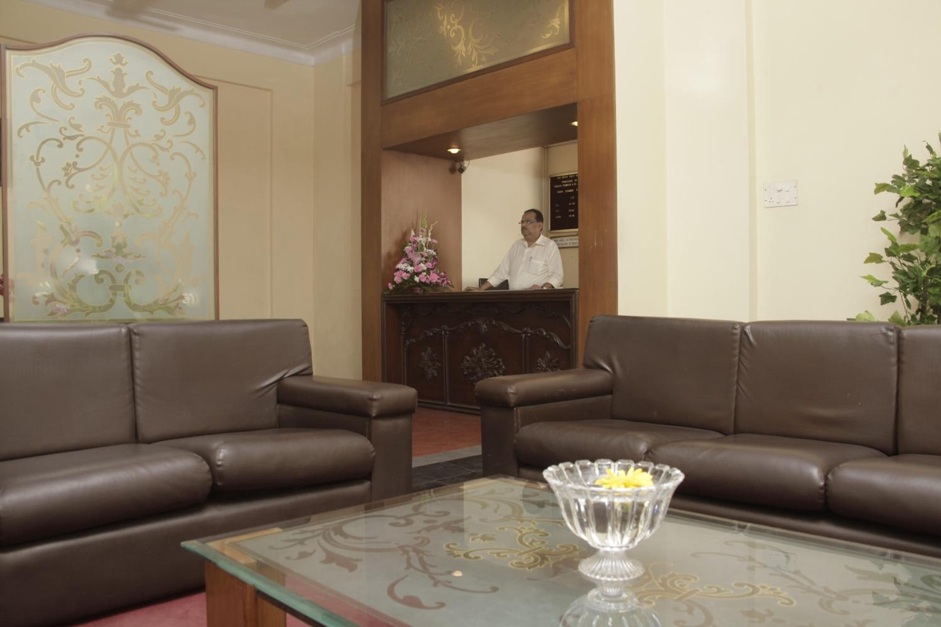 A reception area with a wooden desk, a receptionist, and two brown leather sofas.