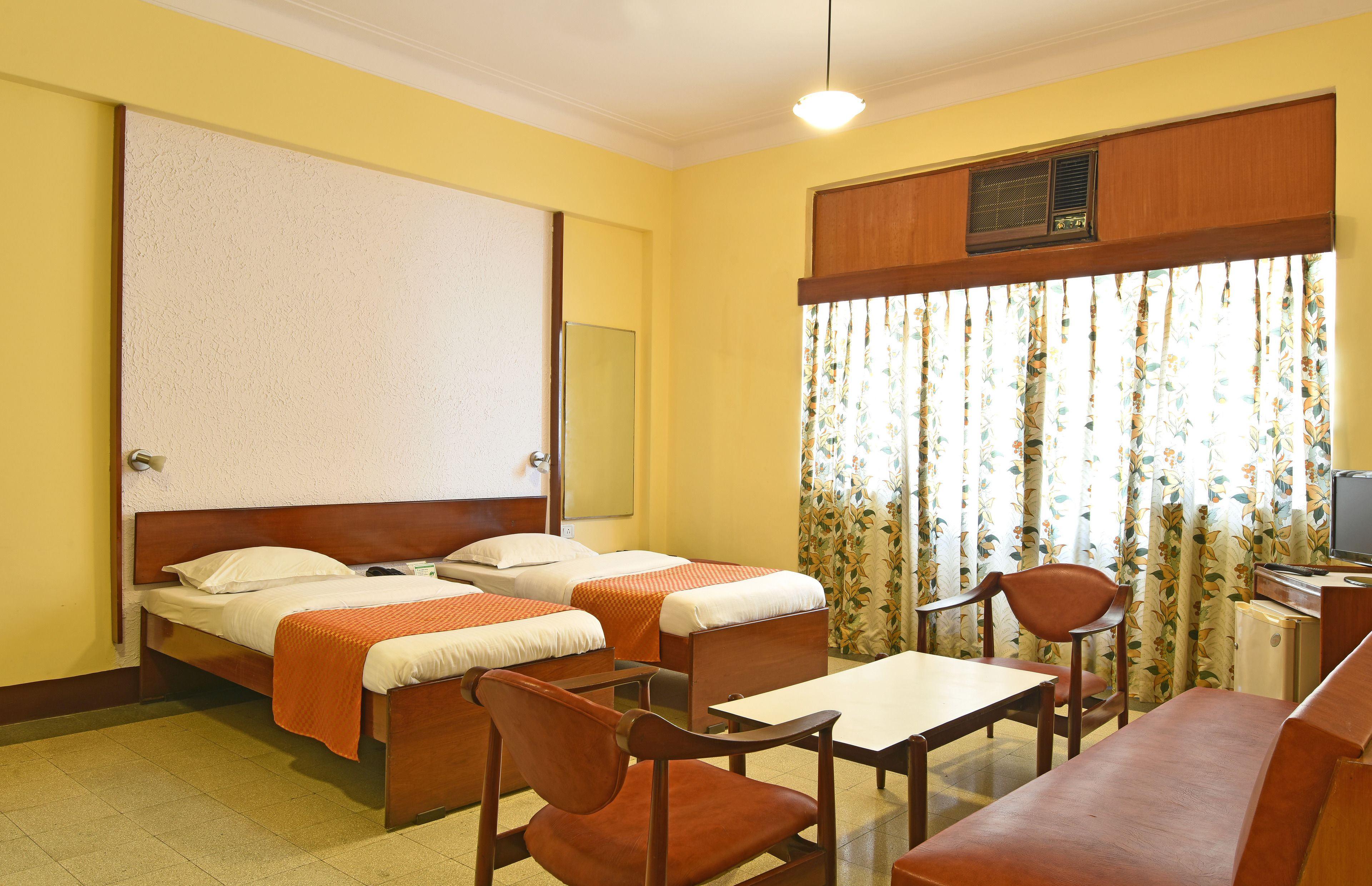 A hotel room with two single beds, a desk with a chair, a television, and a window with curtains.