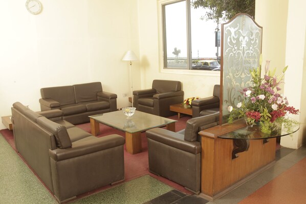 A living room with a brown sofa set, a glass coffee table, and a wooden side table with a vase of flowers. - Sea Green South Hotel (Mumbai)