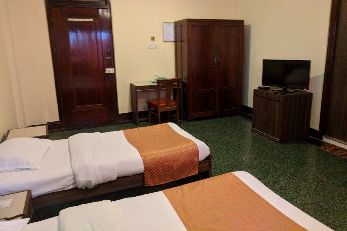 Habitación de hotel con dos camas, un escritorio, una silla, un armario y una televisión.