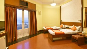 Ein Hotelzimmer mit zwei Betten, einem Schreibtisch, einem Sessel, einem Fernseher und Meerblick durch die Fenster.