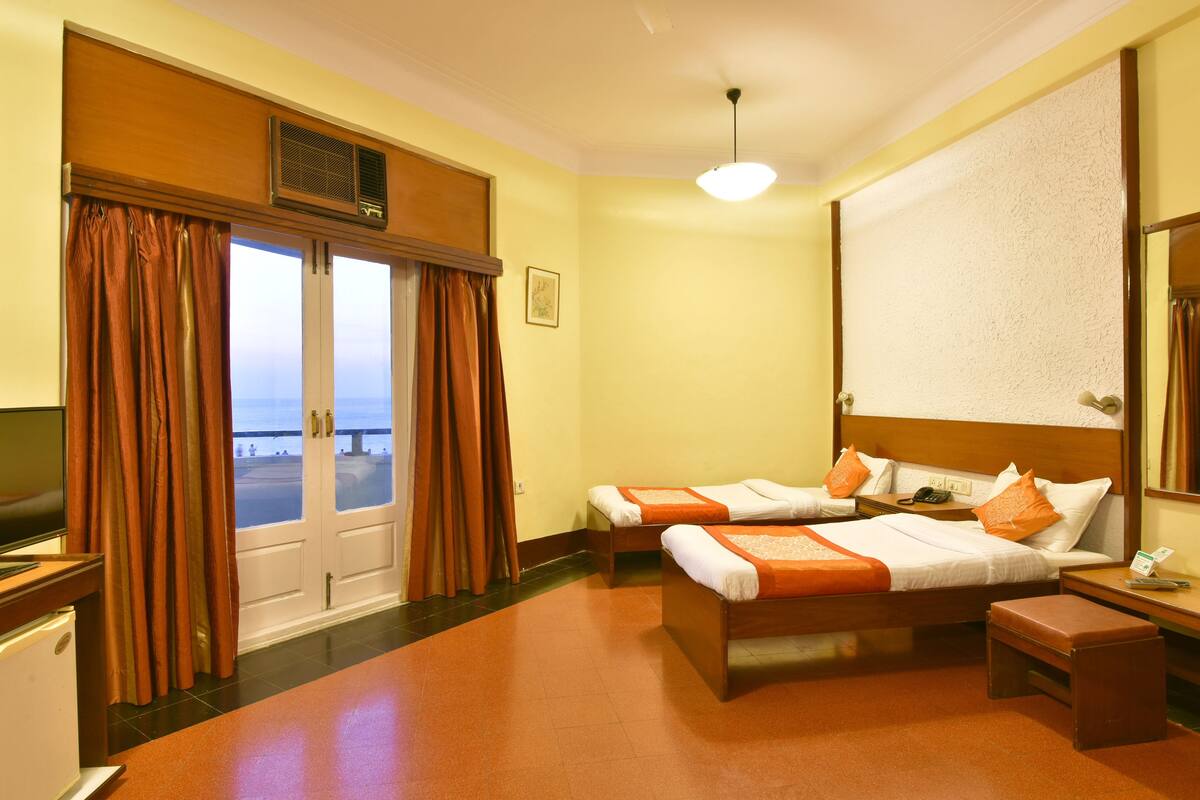 Habitación de hotel con dos camas, un escritorio, una silla, un televisor y vistas al mar a través de las ventanas.