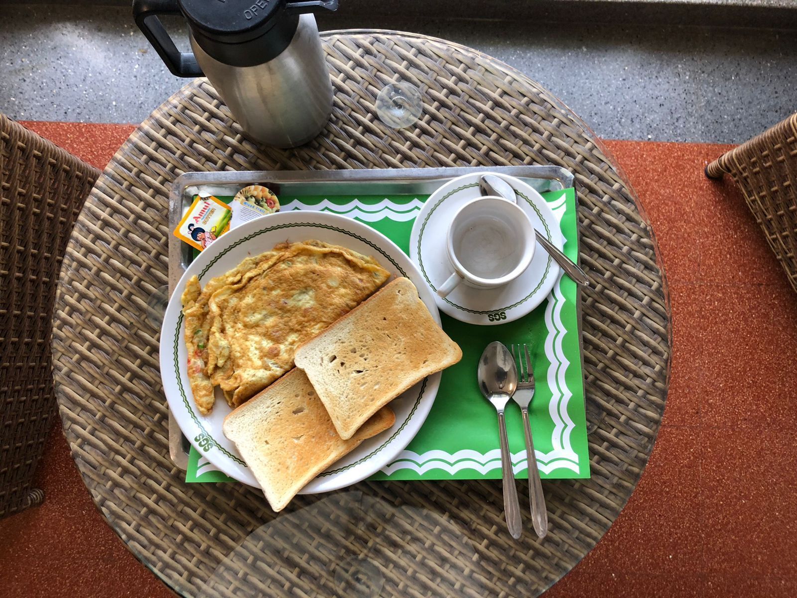 A breakfast setup with a plate of toast and omelette, a cup, and a thermos on a woven mat.
