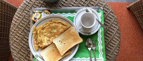 A breakfast setup with a plate of toast and omelette, a cup, and a thermos on a woven mat.