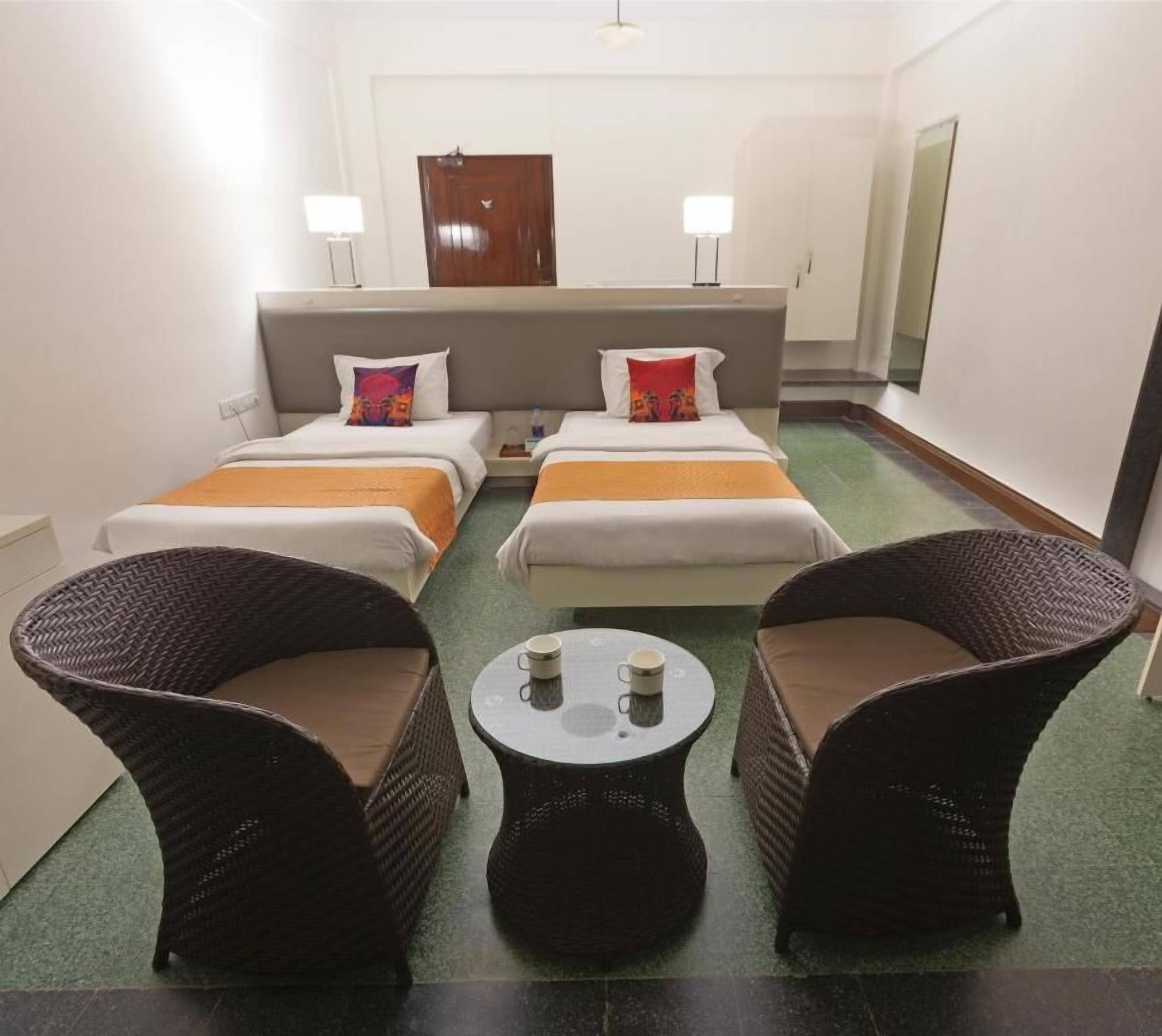 A hotel room with two beds, a sitting area with chairs, a small table, and a mirror on the wall.