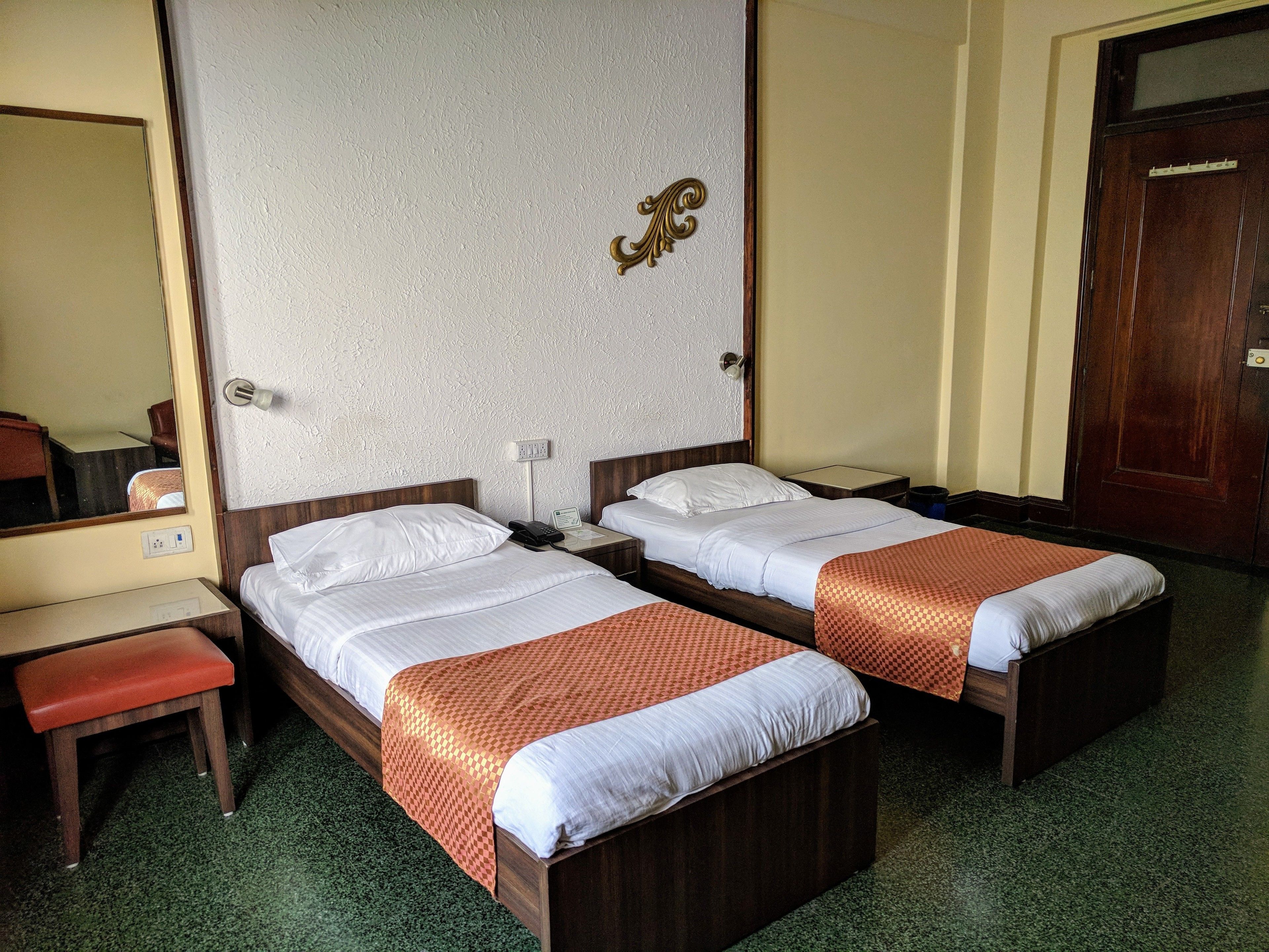 Hotellihuone, jossa on kaksi sänkyä, työpöytä, tuoli ja peili.